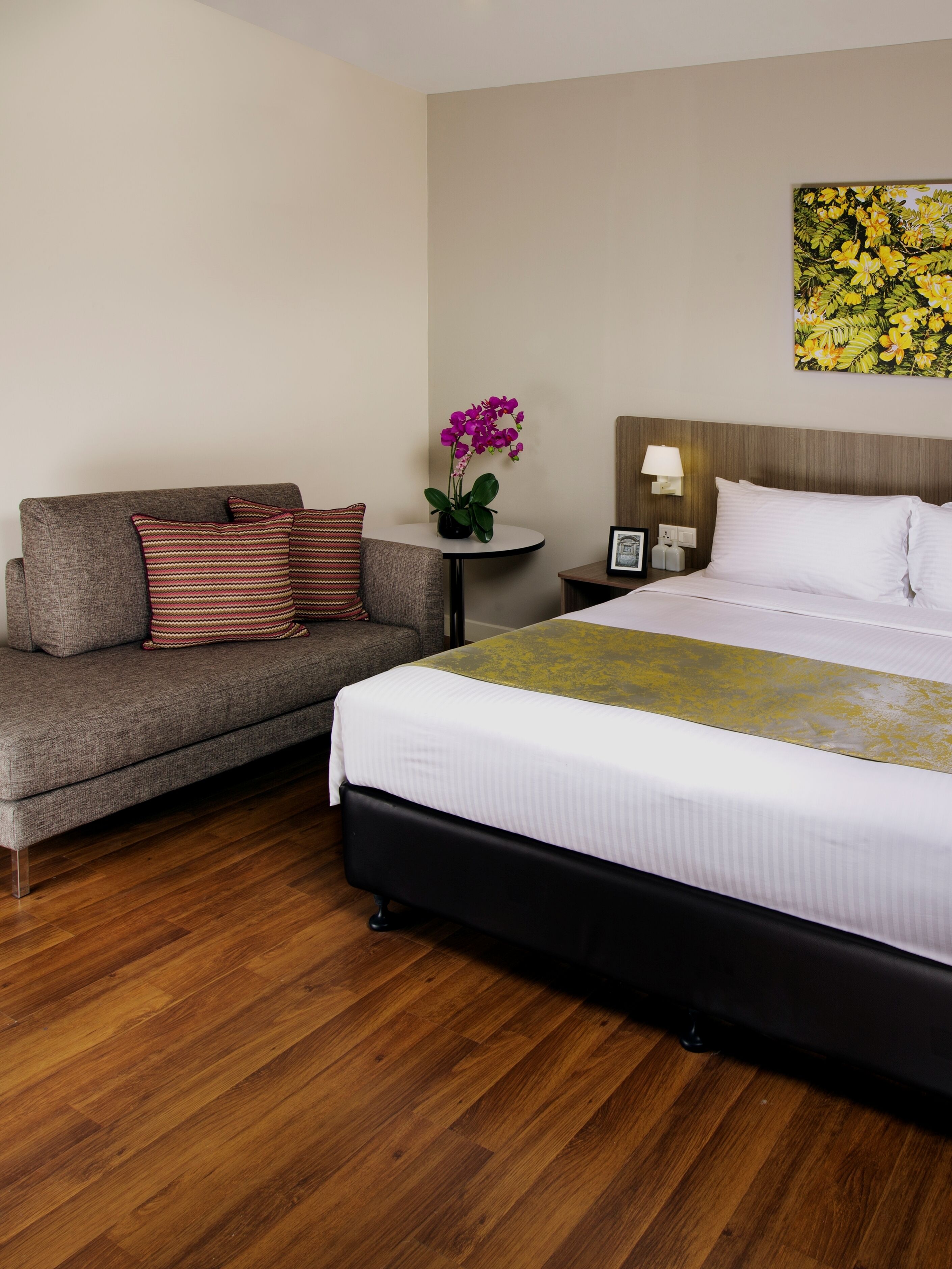 Een hotelkamer met een bed, een bank, een kleine tafel met een bloevas en een schilderij aan de muur.
