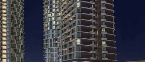 Un edificio de gran altura con múltiples balcones, un paseo cubierto y una zona de piscina.