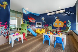 Um espaço de brincadeiras infantil com parede decorada em tema de oceano azul, um escorregador e diversos brinquedos.