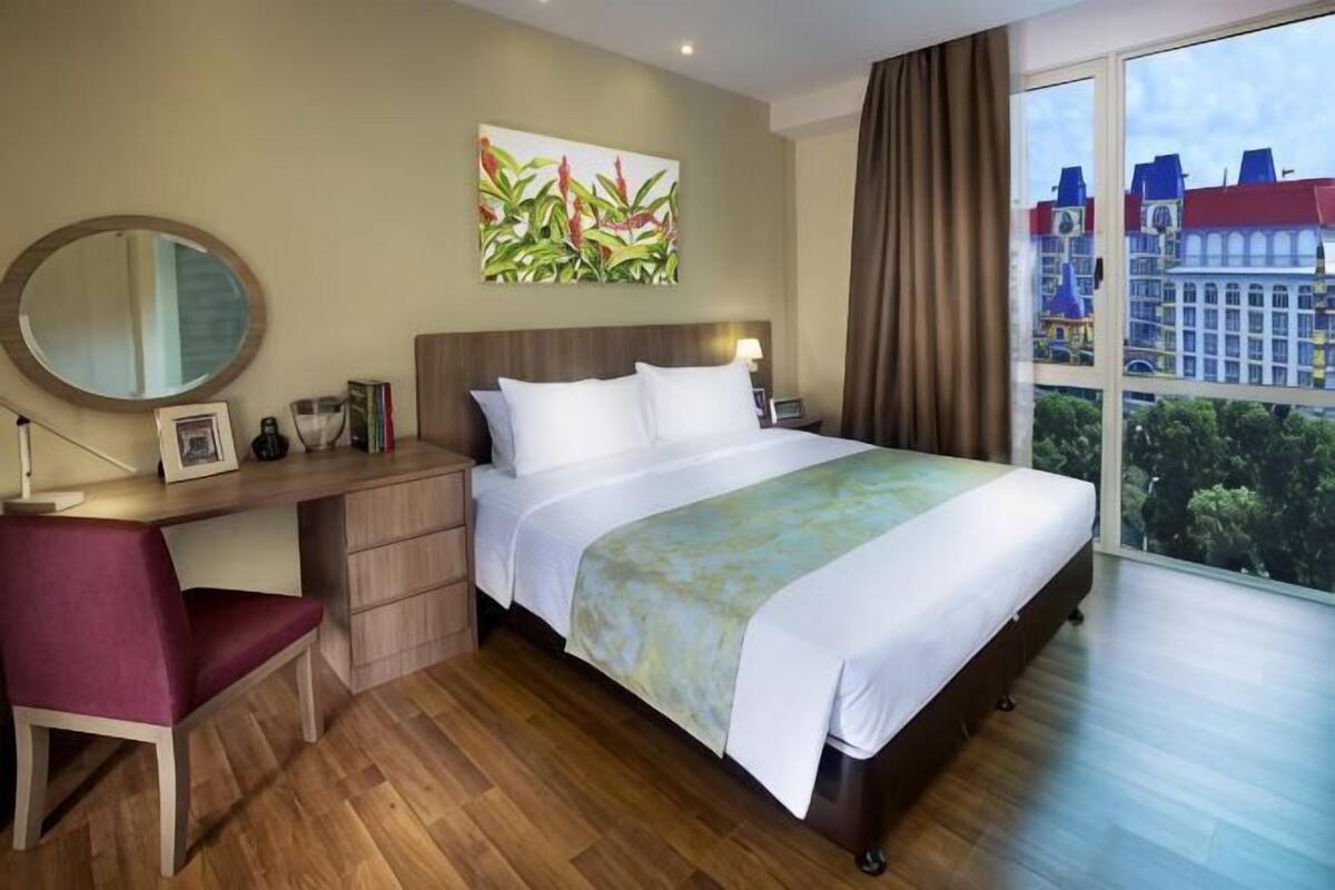 Ein Hotelzimmer mit Bett, Schreibtisch, Stuhl und einem großen Fenster mit Blick auf die Stadt.