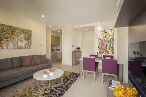 Un salón moderno con sofá, mesa de centro y zona de comedor con sillas. Se observa una cocina al fondo.