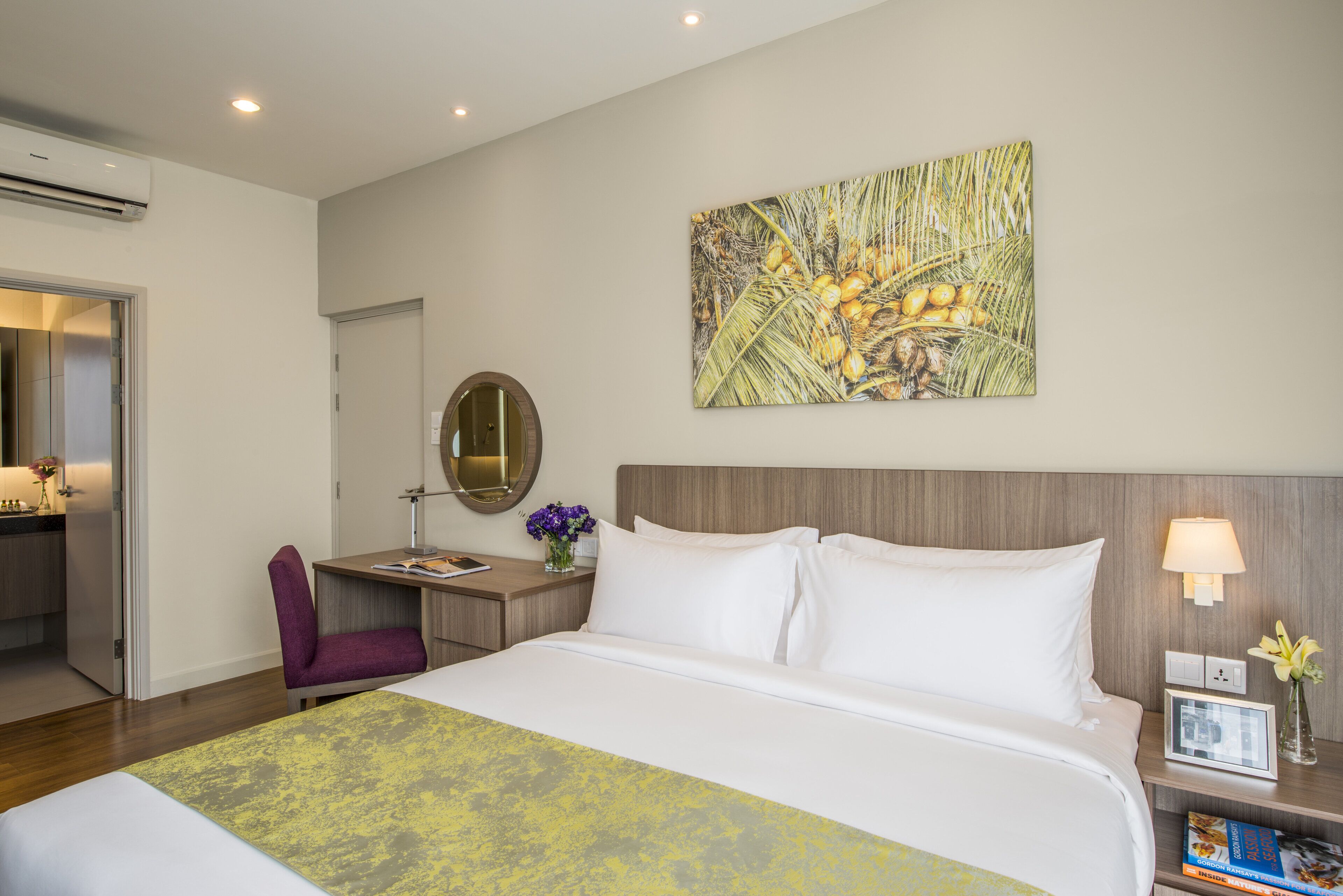 Een hotelkamer met een groot bed, een bureau met stoel, een nachtkastje met lamp en een aan de muur hangend kunstwerk.