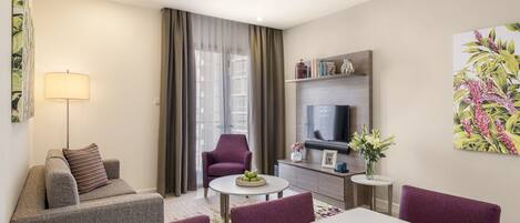 Una sala de estar moderna con un sofá, sillones, una mesa de comedor con manzanas, un televisor y una chimenea.