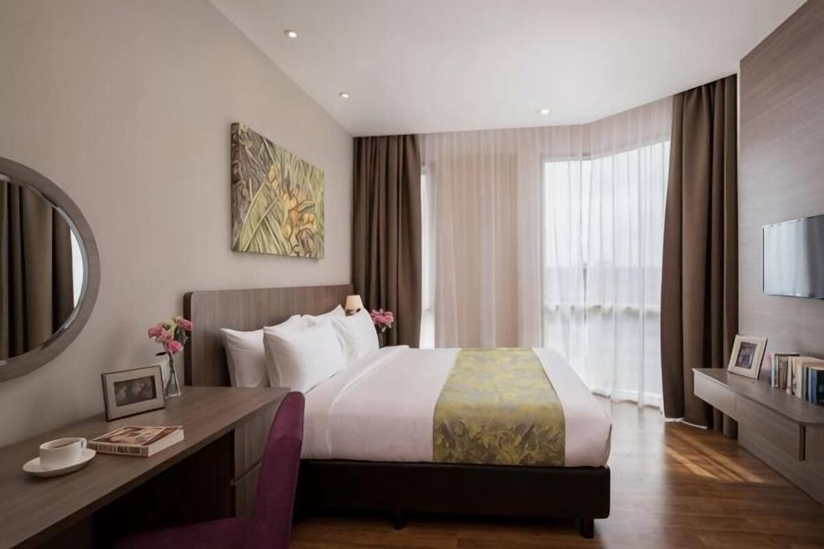 Ein Hotelzimmer mit Bett, Schreibtisch, Stuhl, Fernseher, einem Bild und einem Fenster mit Vorhängen.