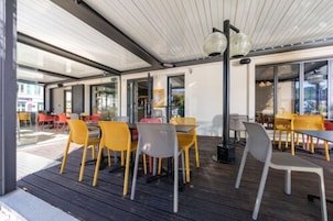 Uma área de refeições interna com mesas e cadeiras, janelas amplas e um teto com design em painéis de madeira.