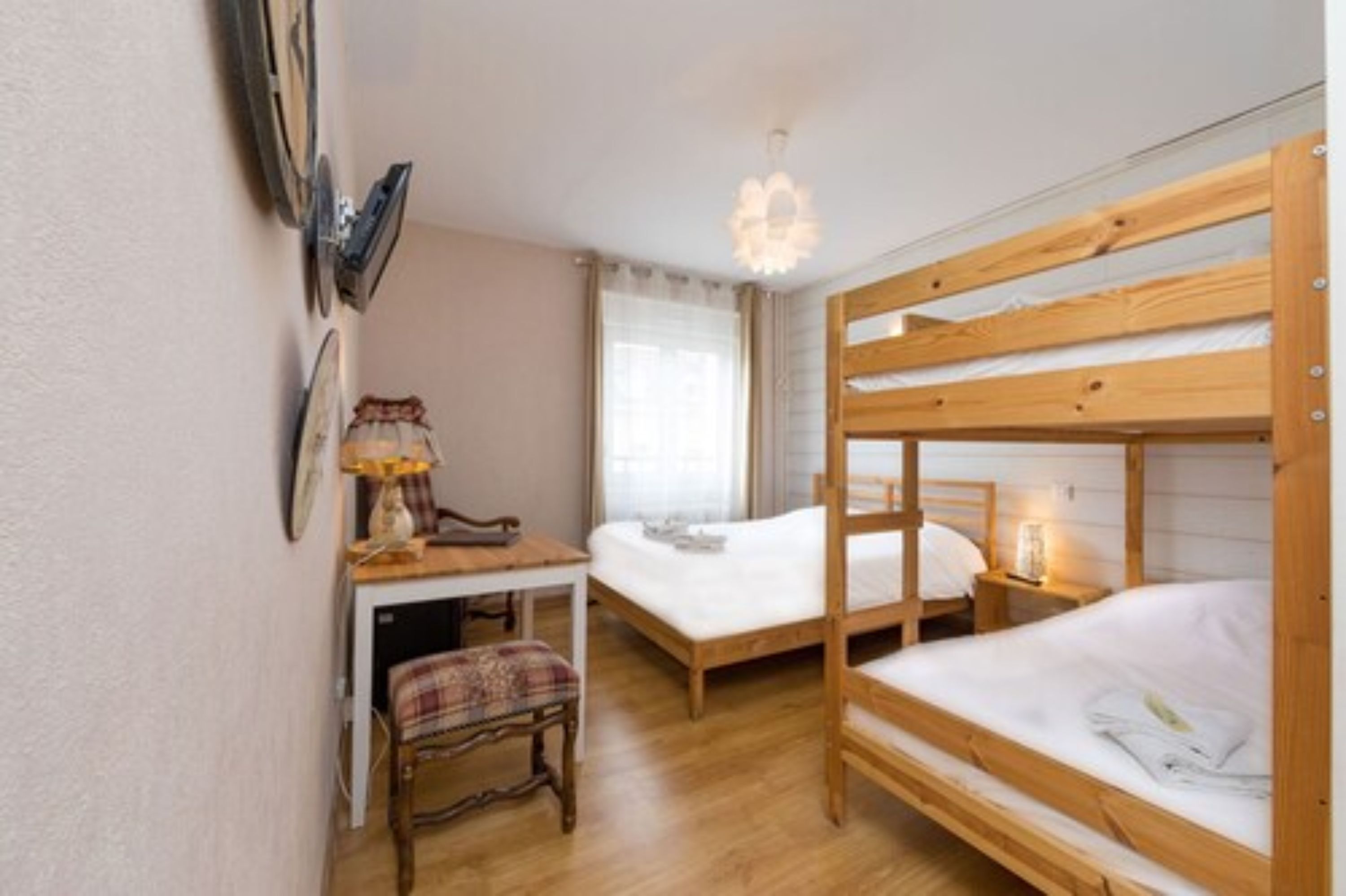 Et lille, hyggeligt værelse med to køjesenge, et skrivebord med stol og en lampe.
