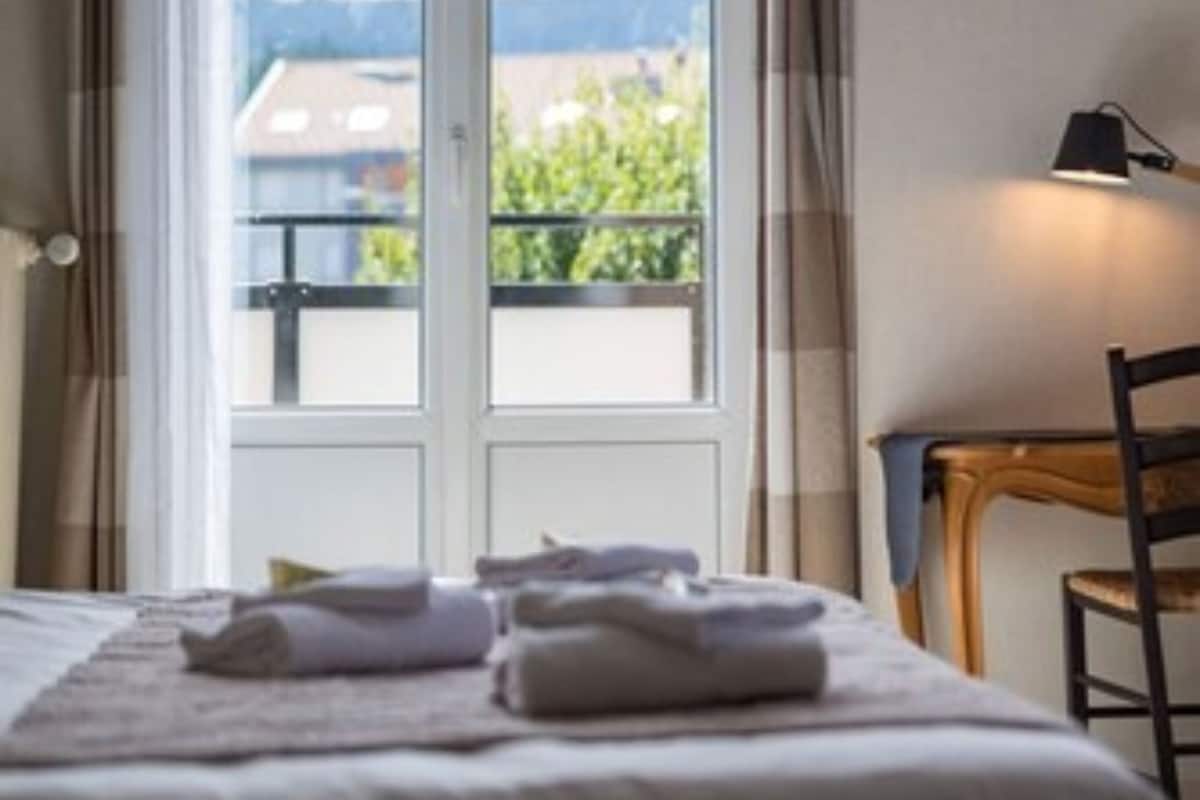 Una habitación de hotel con cama, una silla, un escritorio y una ventana con cortinas.