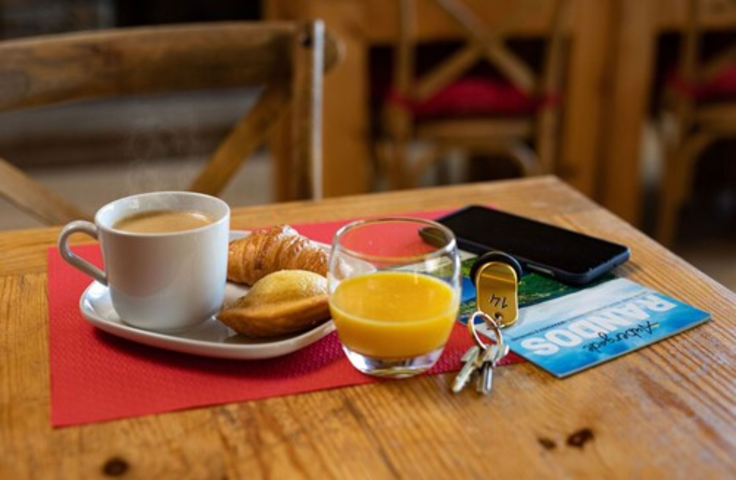 A breakfast setting with a cup of coffee, croissants, a glass of orange juice, a smartphone, and a Panama card on a wooden table.