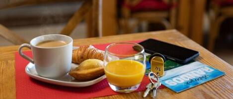 A breakfast setting with a cup of coffee, croissants, a glass of orange juice, a smartphone, and a Panama card on a wooden table.