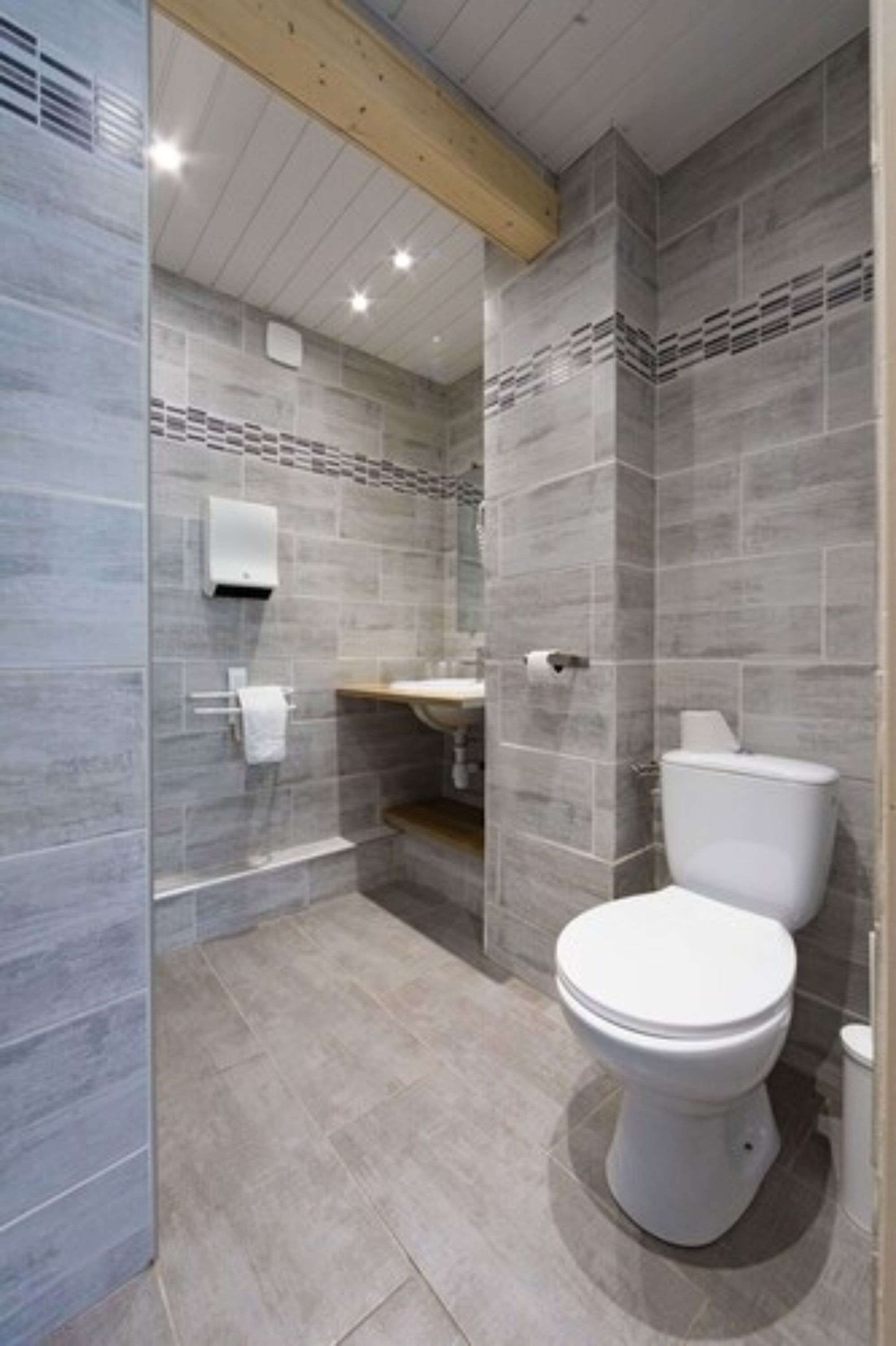 A modern bathroom with grey tiles, a white toilet, a sink, and a shower area.