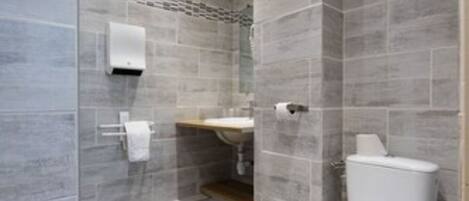A modern bathroom with grey tiles, a white toilet, a sink, and a shower area.