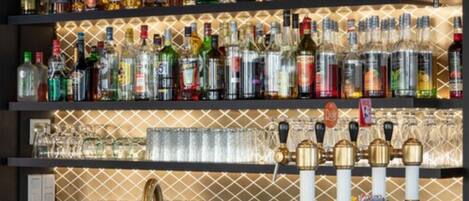 A bar area with shelves of liquor bottles and glasses, a tap with a gold faucet, and a patterned wall in the background.