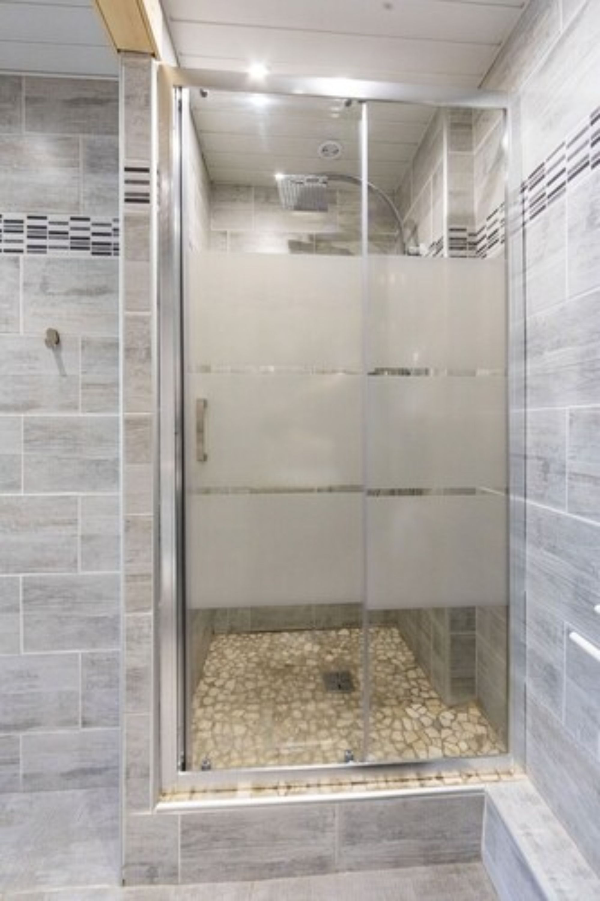 Una ducha con puerta de vidrio, paredes de azulejos y suelo de piedra.