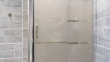 A shower with a glass door, tiled walls, and a stone floor.