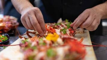 Eine Person bereitet Essen zu, vermutlich ein Fischgericht, wobei Zutaten wie Krabben, Kräuter und möglicherweise Gemüse sichtbar sind.