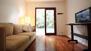 A living room with a beige sofa, a TV on a wooden stand, and a door leading to a garden. - Gomide SP 21 (São Paulo)