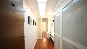 A hallway with wooden flooring, white walls, and a ceiling light. There are framed pictures on the wall and a door with a handle. - Gomide SP 21 (São Paulo)