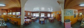 A spacious dining area with multiple tables and chairs, wooden walls, and a high ceiling with skylights. - Pousada Fazenda Recanto dos Carvalhos (Pouso Alto)