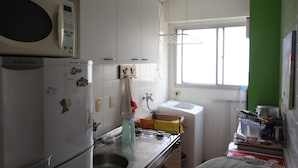 Een compacte keuken met een magnetron, koelkast, spoelbak en een raam dat natuurlijk licht binnenlaat.