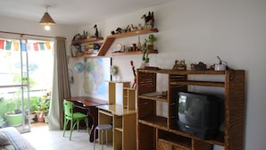 Een woonkamer met een televisie, houten planken, een bureau, een stoel en een eettafel.