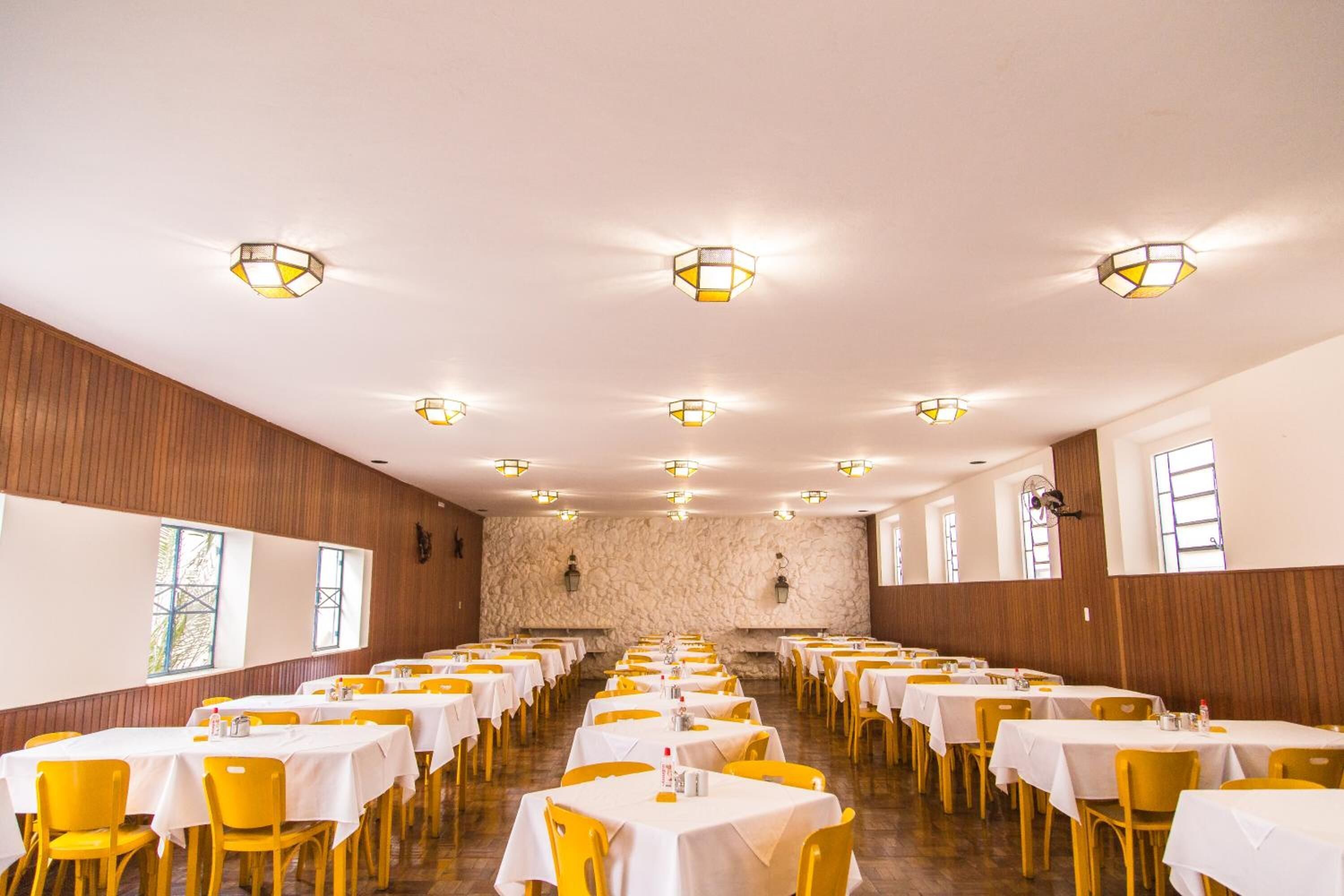 A large banquet hall with rows of tables and chairs, stone walls, and ceiling lights.