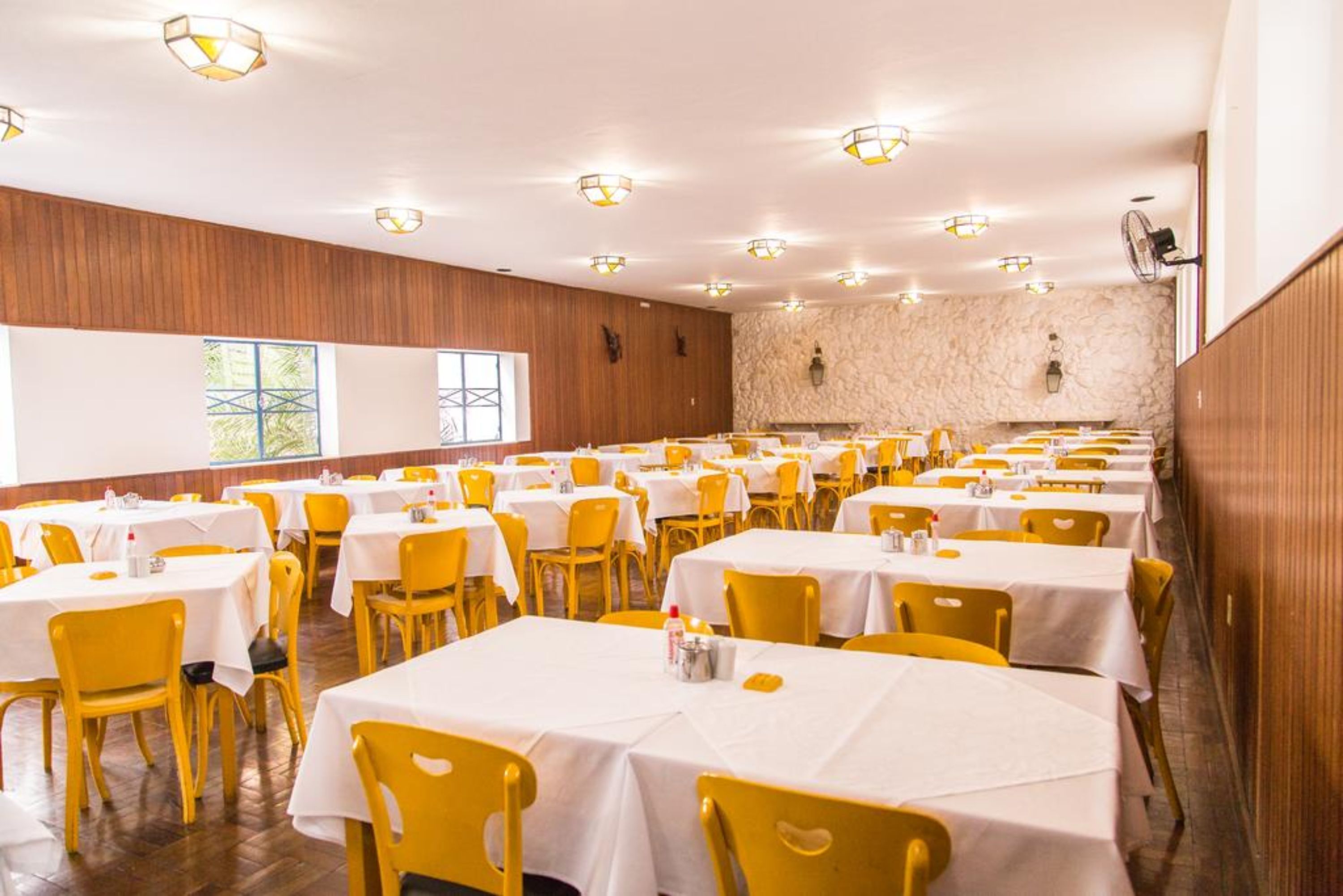 Un salón de banquetes con varias mesas redondas cubiertas con manteles blancos y sillas amarillas.