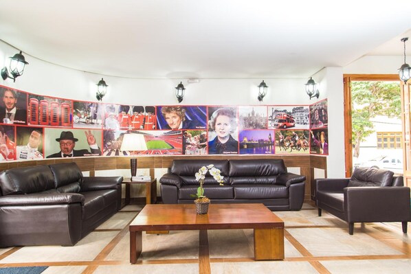 Un vestíbulo con una pared curva decorada con diversos carteles, un sofá de cuero negro, una mesa de centro de madera y una orquídea en maceta.