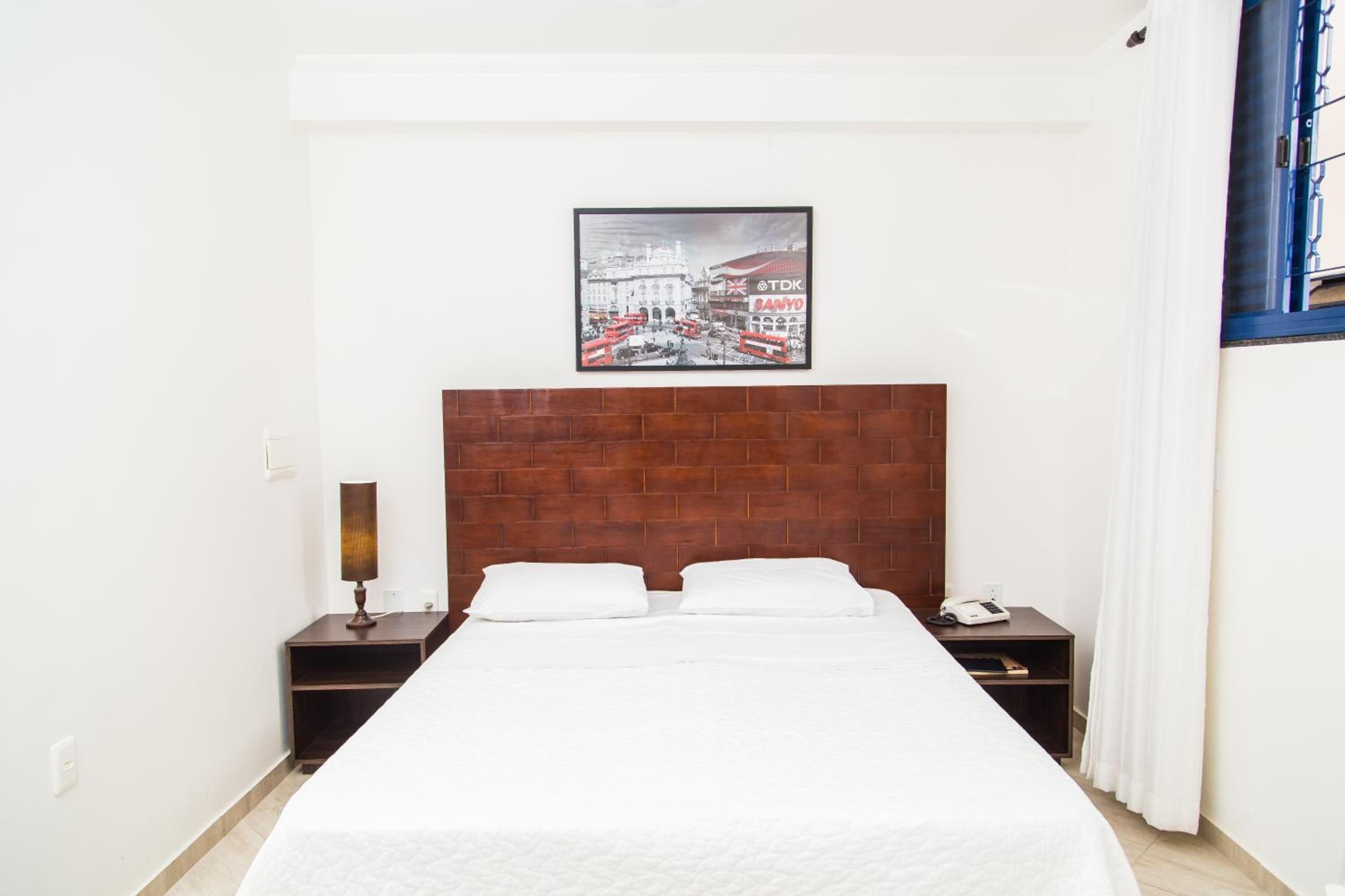 Ein Hotelzimmer mit einem großen Bett, einem hölzernen Kopfteil, einem Nachttisch mit Lampe und einem gerahmten Bild an der Wand.