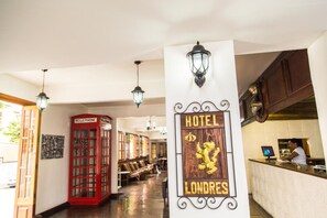Un vestíbulo de hotel con un teléfono rojo, una recepción y un letrero con el nombre del hotel.