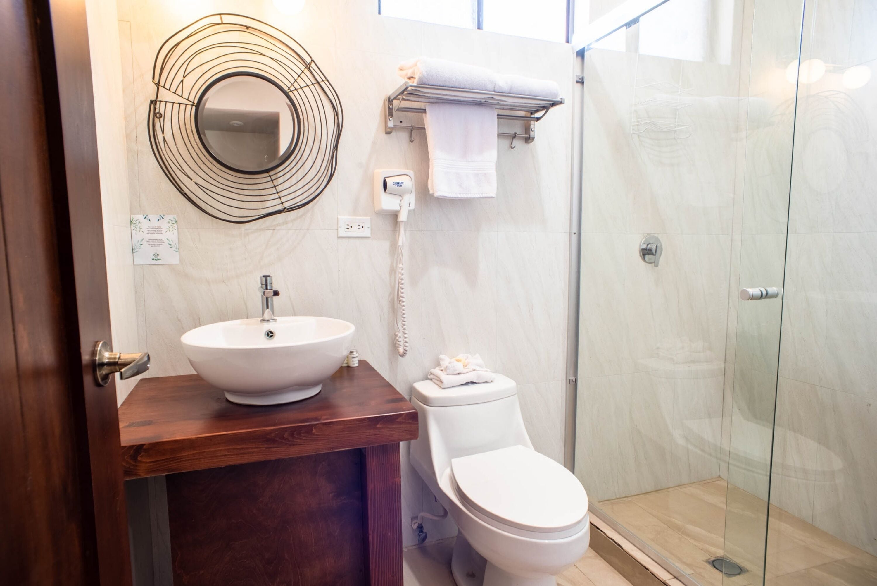 Une salle de bain avec un meuble-lavabo en bois, un lavabo blanc, des toilettes, une cabine de douche en verre et un porte-serviettes.