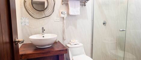 Une salle de bain avec un meuble-lavabo en bois, un lavabo blanc, des toilettes, une cabine de douche en verre et un porte-serviettes.