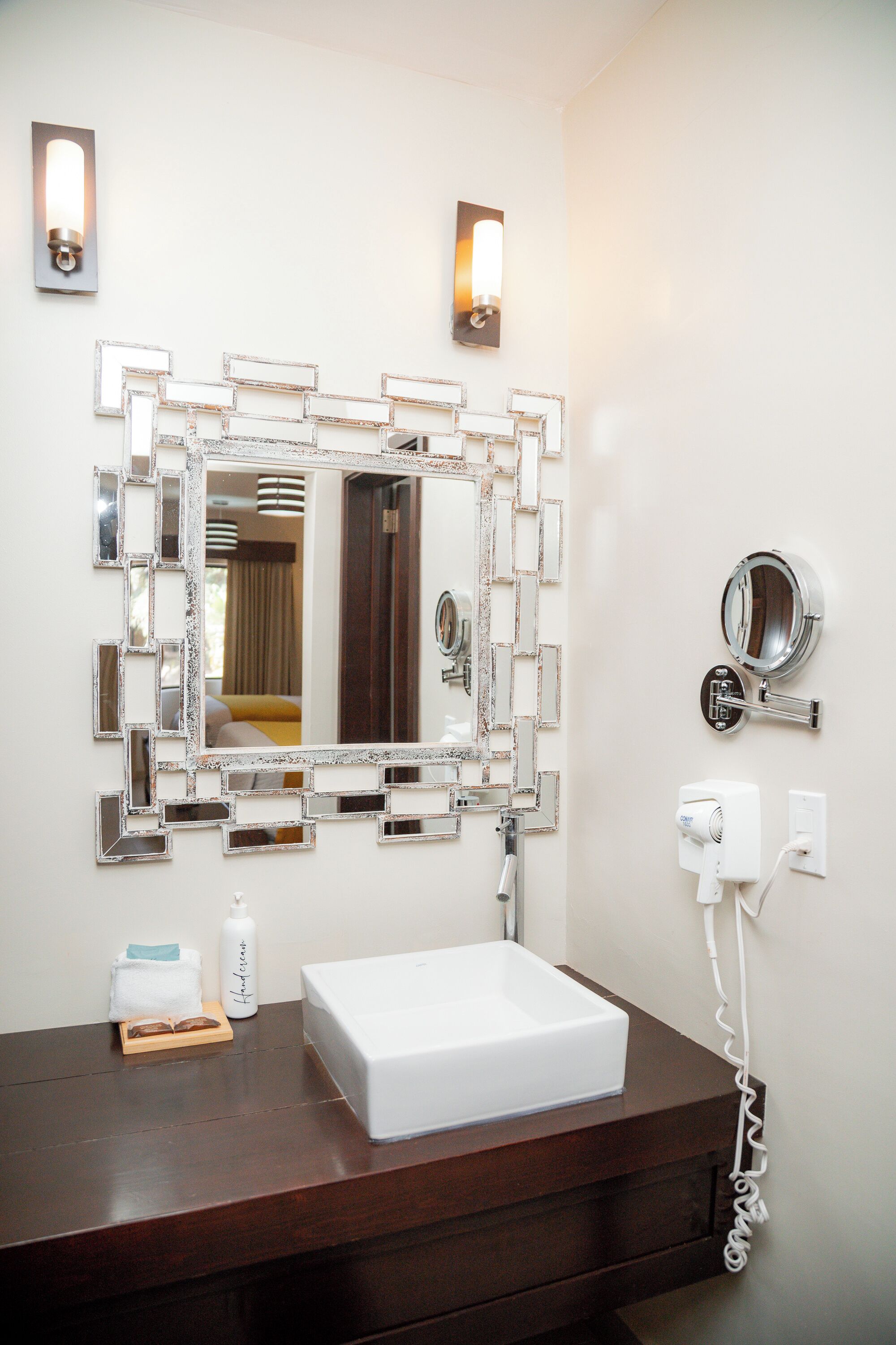 Un baño con un espejo grande, un lavabo blanco, un espejo de mano y un secador de pelo.