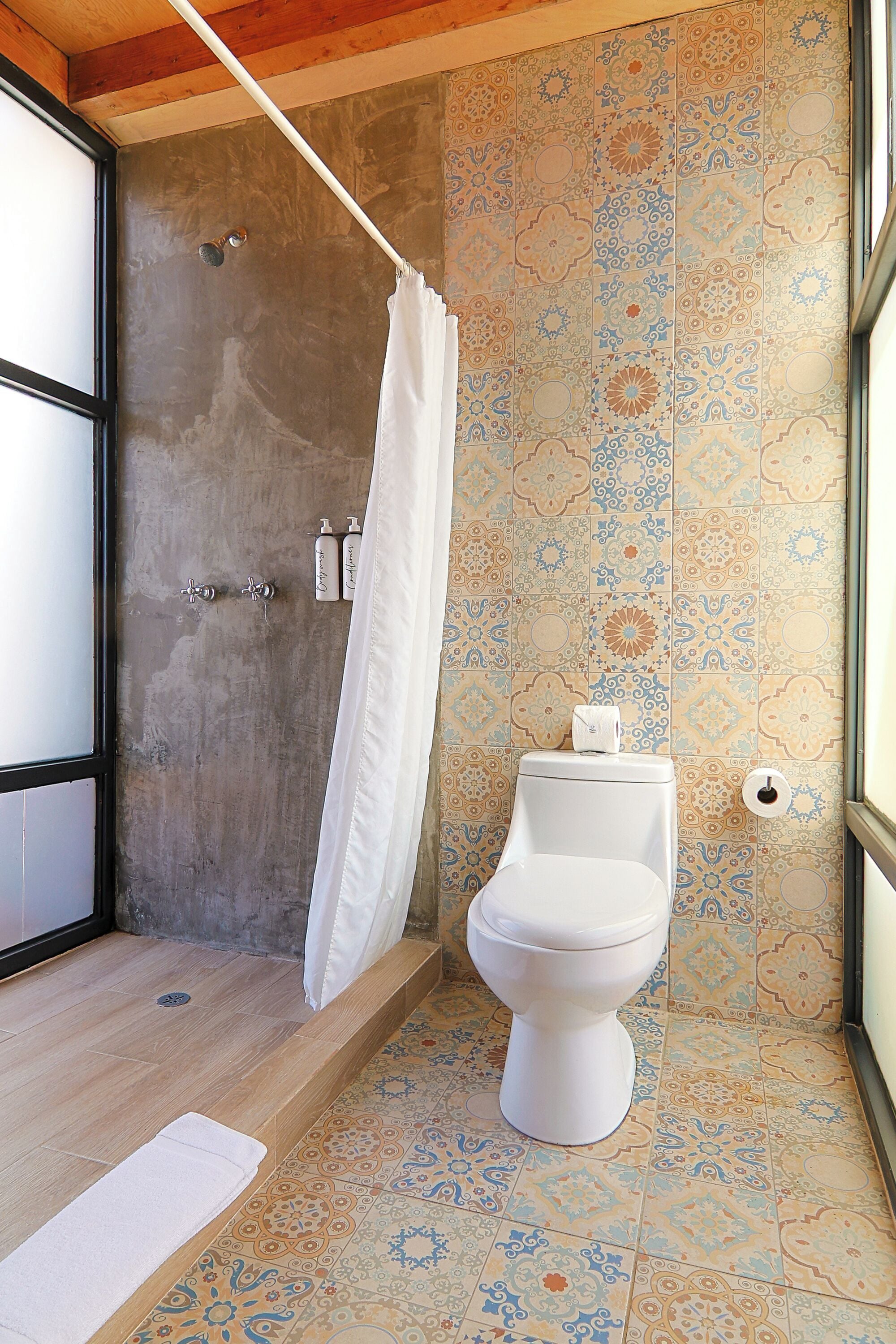 Un baño con ducha, inodoro y azulejos estampados.