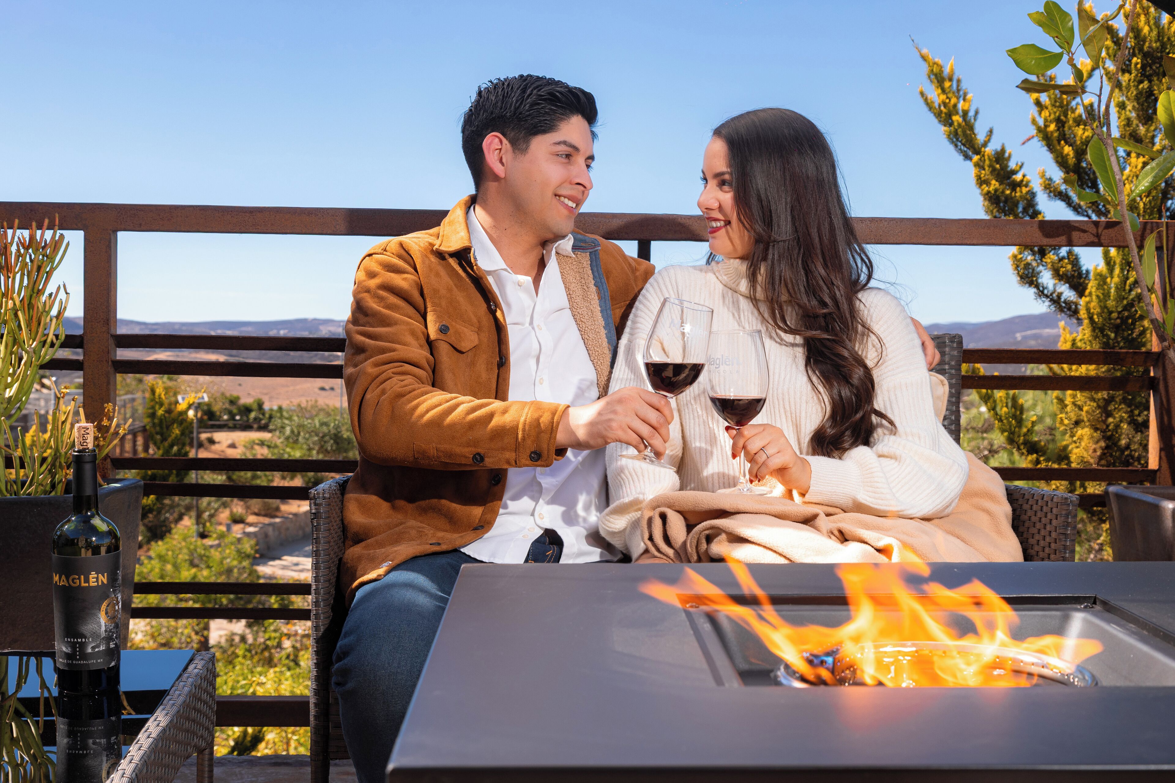 A couple sitting at a table with a fire feature, overlooking a scenic landscape.