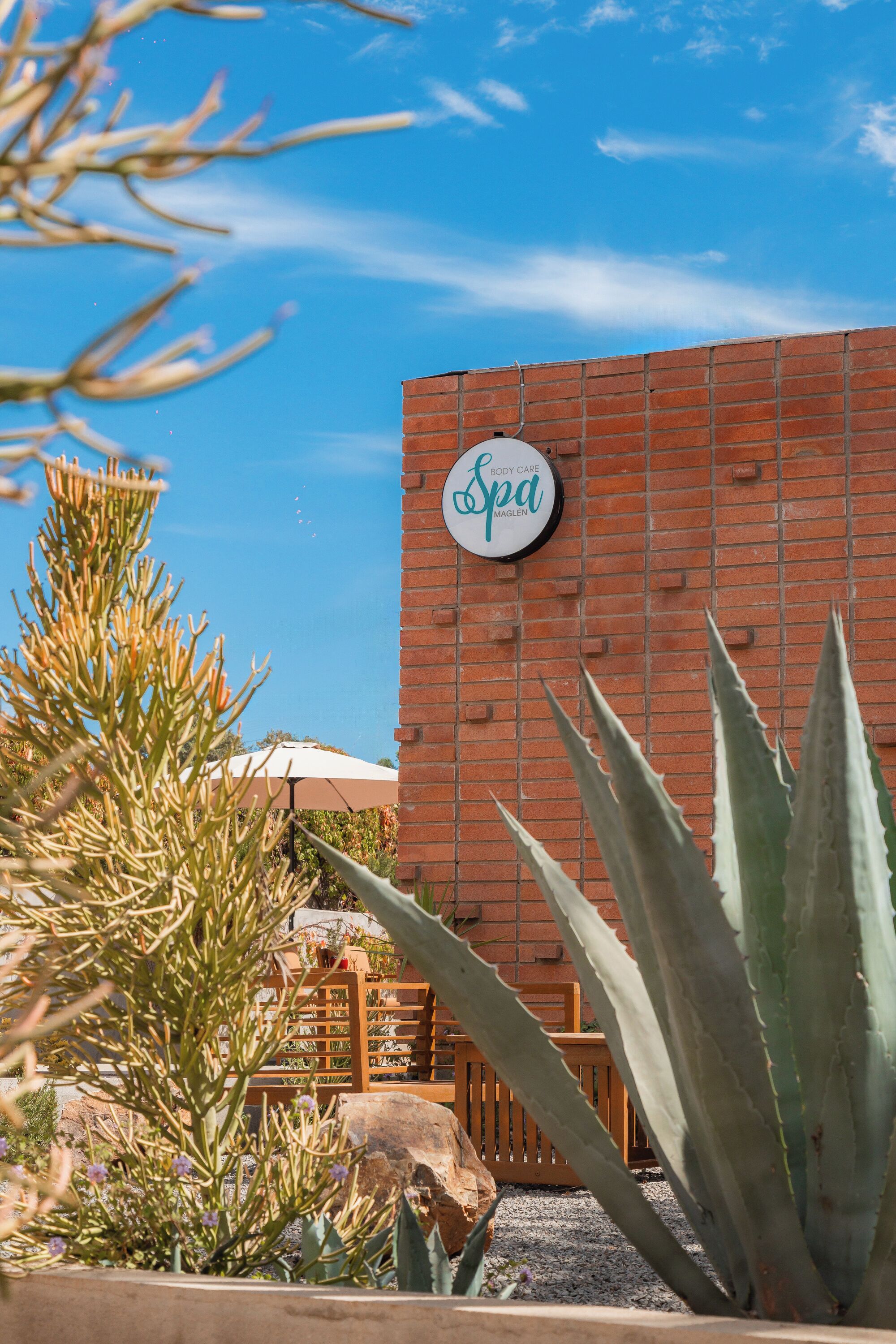 A spa sign on a brick wall with cacti and a wooden fence in the foreground.