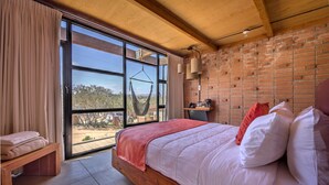 Quarto com cama grande, rede, um banquinho e vista para o exterior.