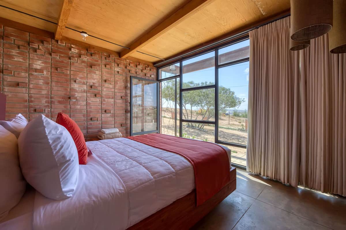 Ein Schlafzimmer mit einem großen Bett, einer Ziegelwand und Blick ins Freie.