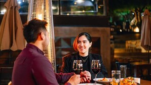 Um casal jantando em restaurante, mesa posta para dois, copos de vinho e pratos de comida.