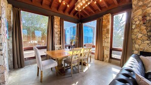 A dining area with a wooden table and chairs, stone walls, and large windows with curtains.