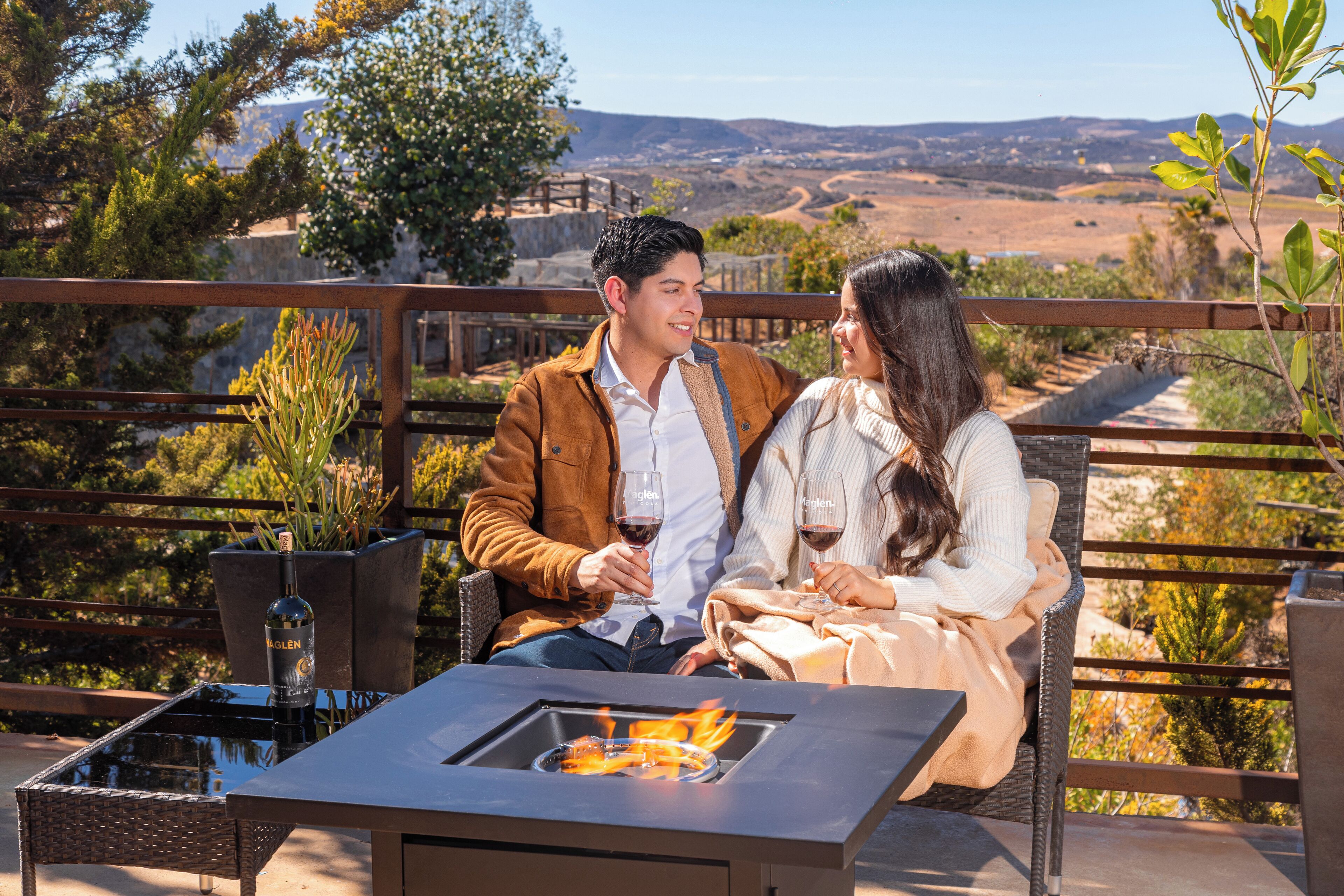 Una pareja sentada en una mesa al aire libre con una chimenea integrada, con vistas a un paisaje pintoresco.