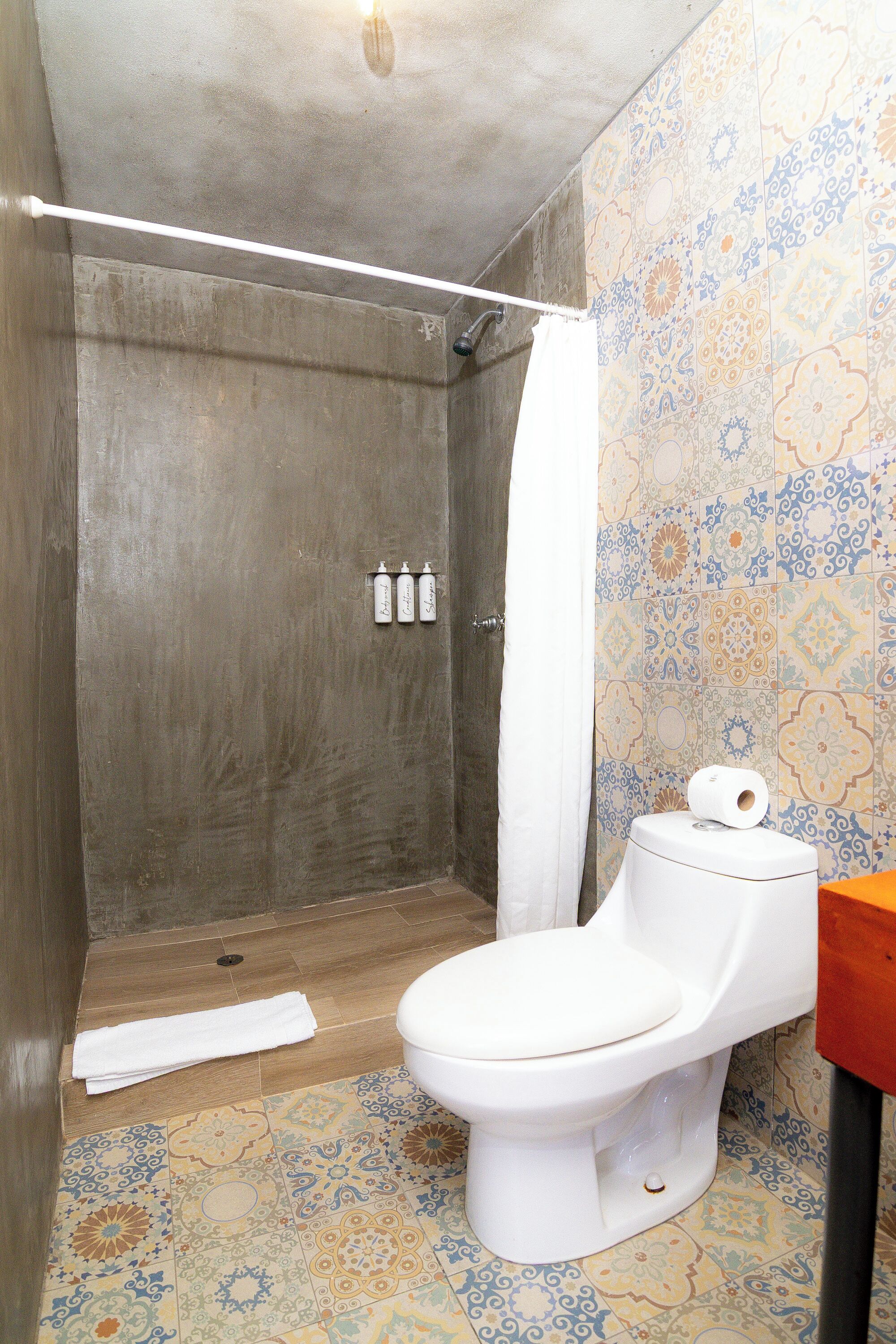 Un baño con ducha, inodoro y azulejos estampados.