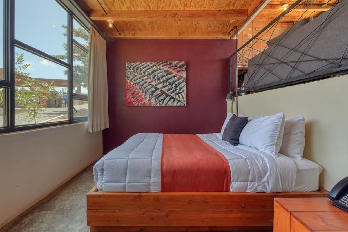 Ein Schlafzimmer mit einem hölzernen Bett, einer roten Decke und einem Gemälde an der Wand.