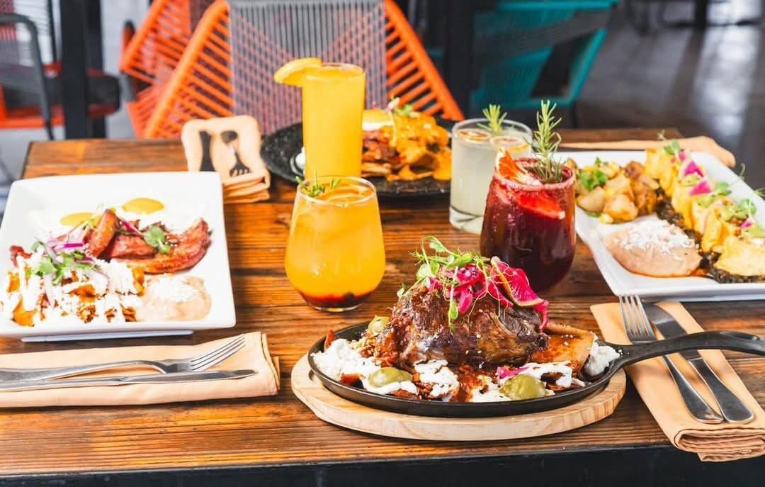 A wooden table with various dishes, including grilled meat, salads, and drinks.