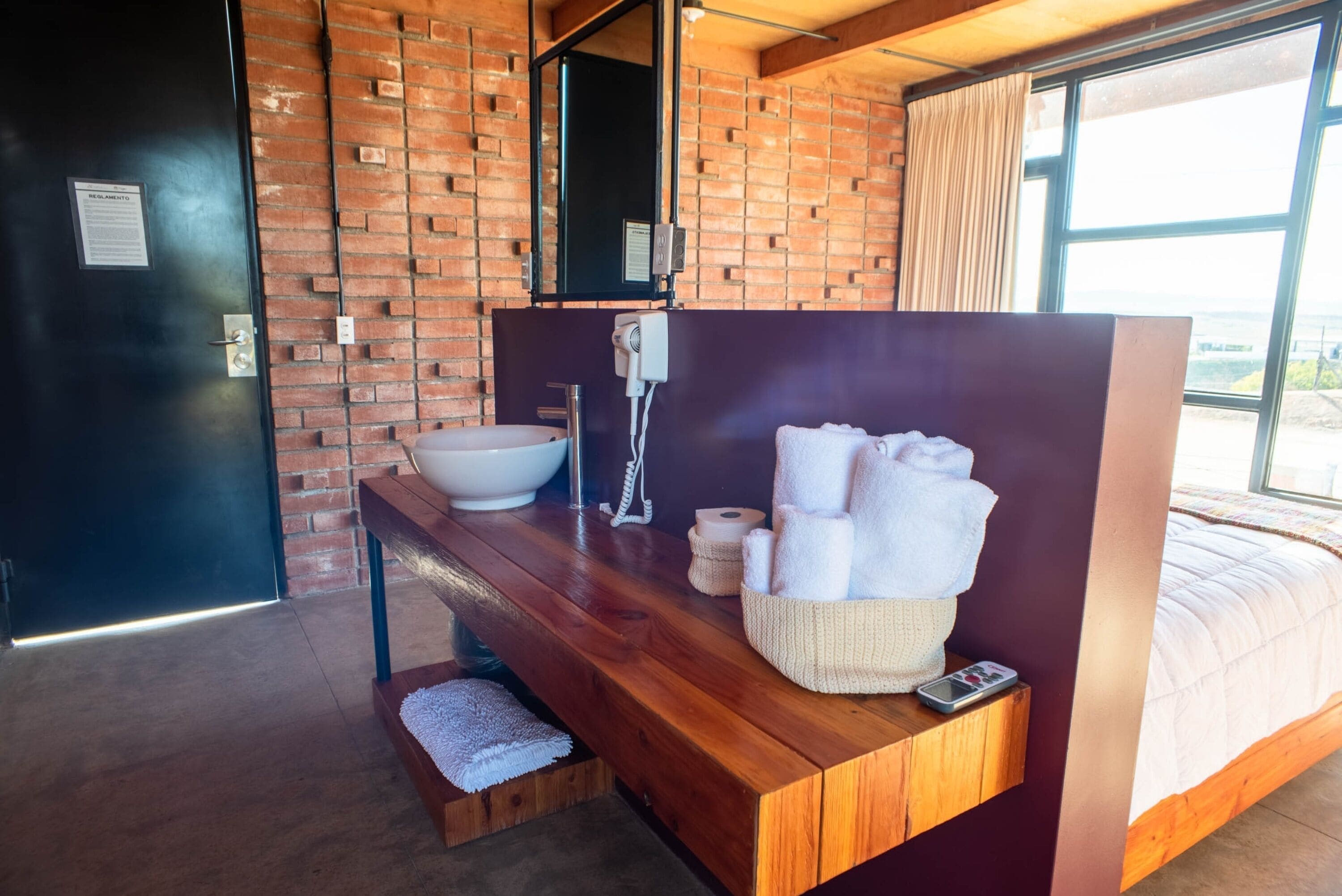 A modern bathroom with a wooden vanity, a large sink, and a mirror. There is a towel rack with towels and a small basket.