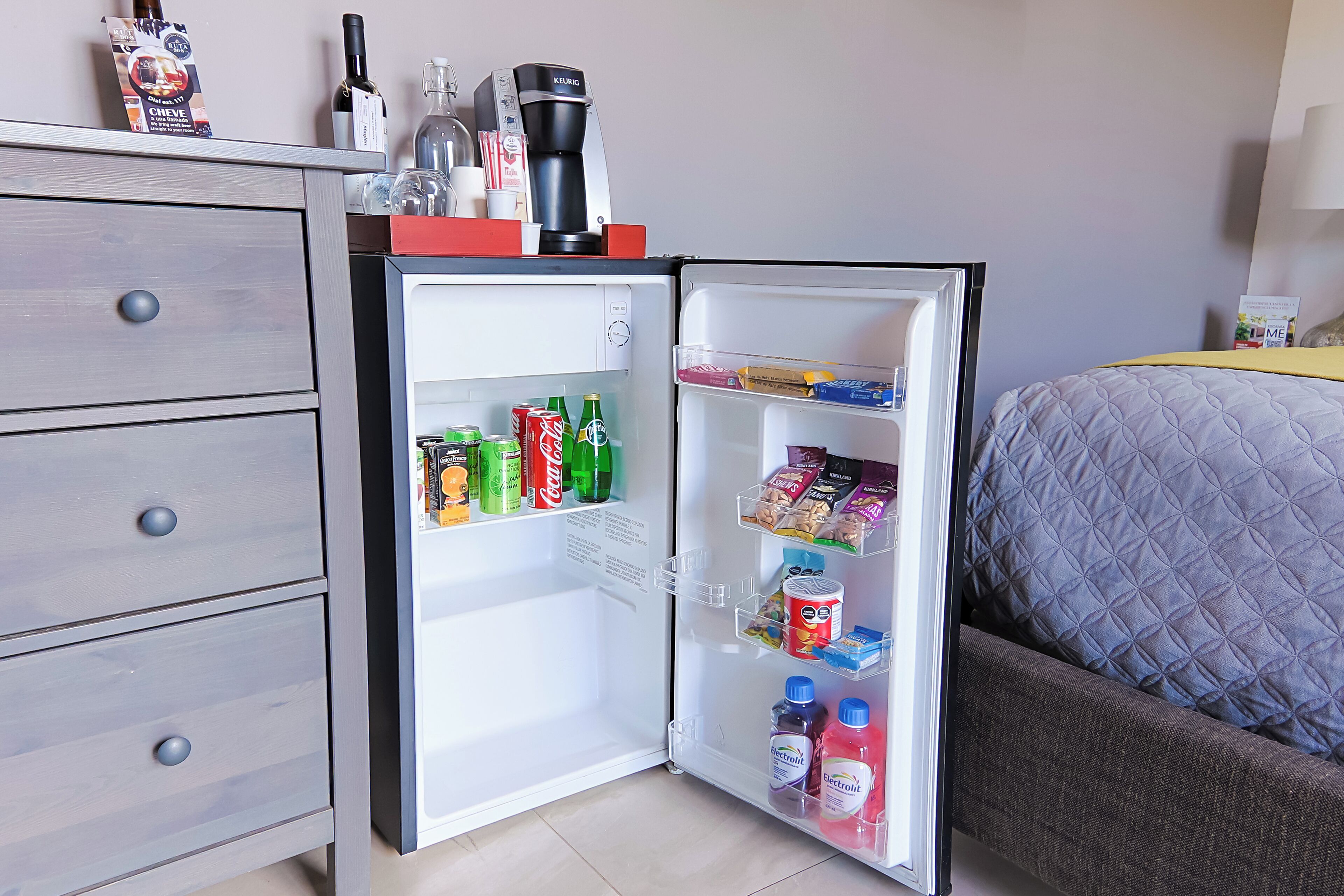 A compact refrigerator with a coffee maker and a wine bottle on top, stocked with beverages and snacks.