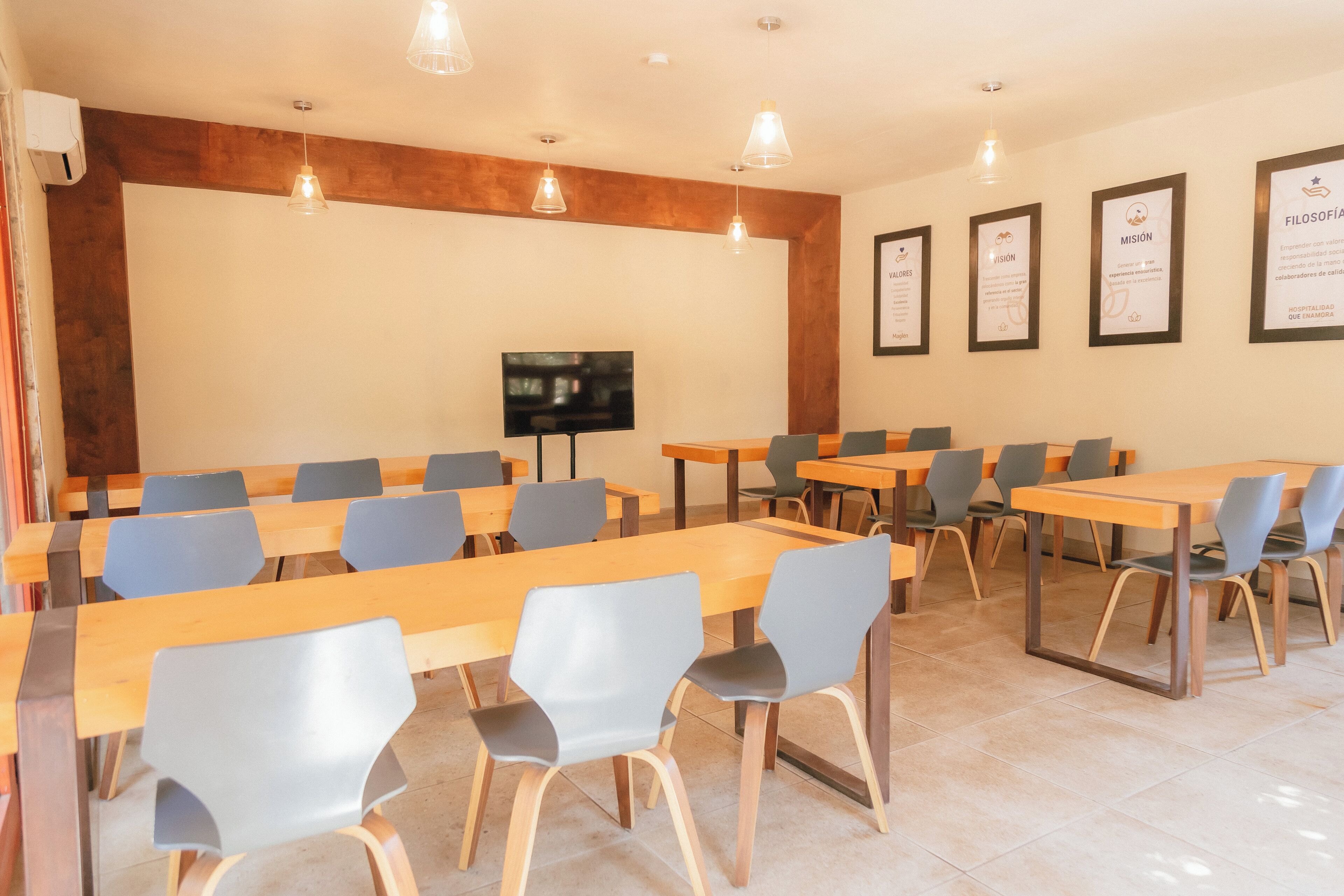 A conference room with tables and chairs, a flat-screen TV, and framed certificates on the wall.