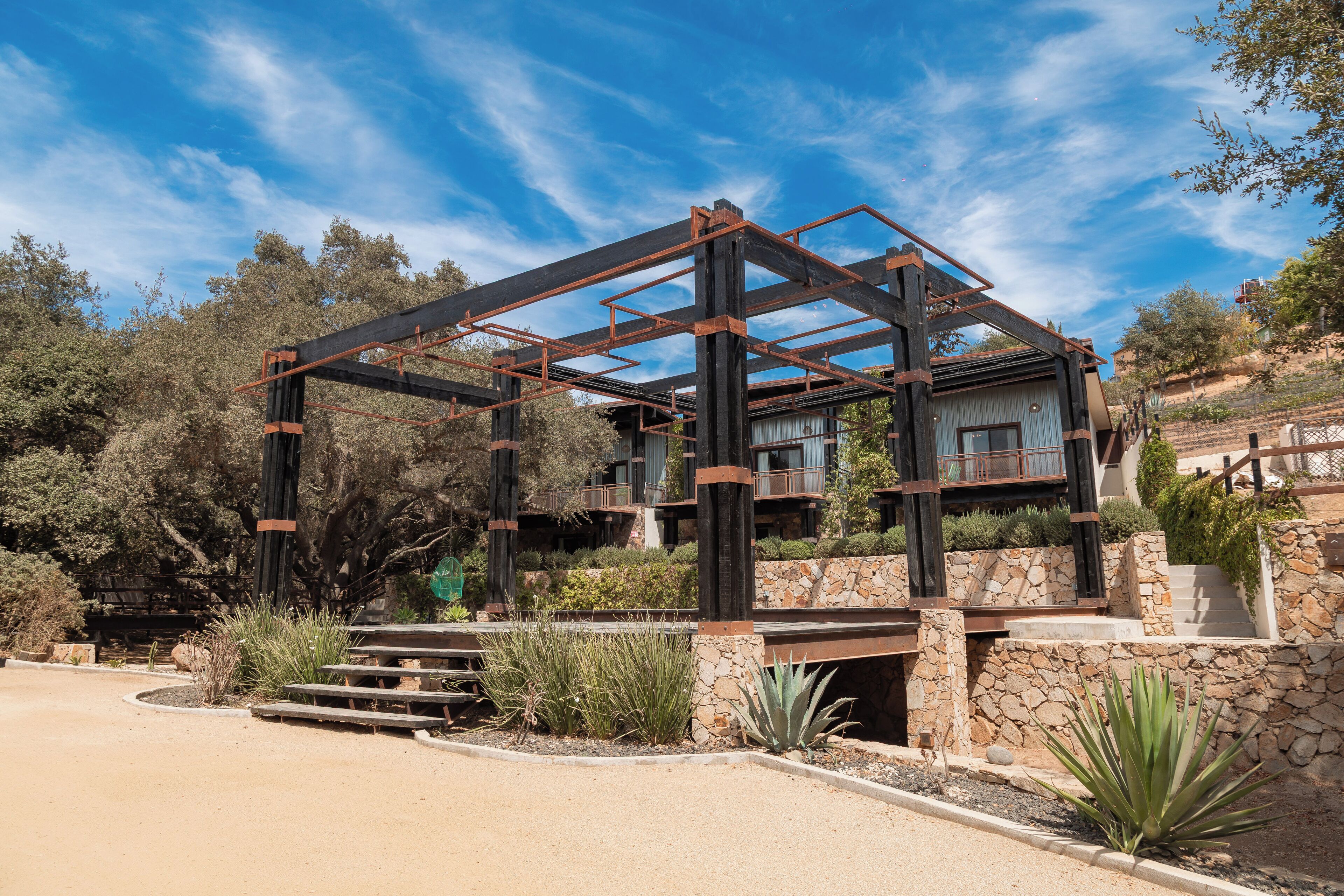 Una casa moderna con estructura metálica, paredes de piedra y vistas al paisaje circundante.