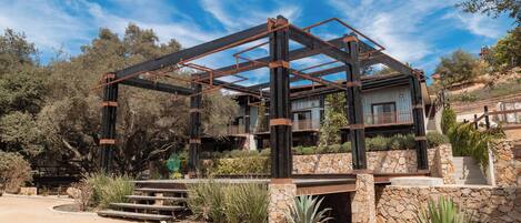 Una casa moderna con estructura metálica, paredes de piedra y vistas al paisaje circundante.