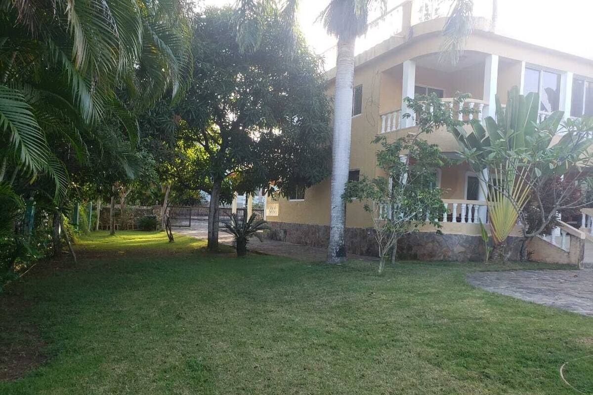 A building with a balcony, surrounded by a grassy lawn and various trees.