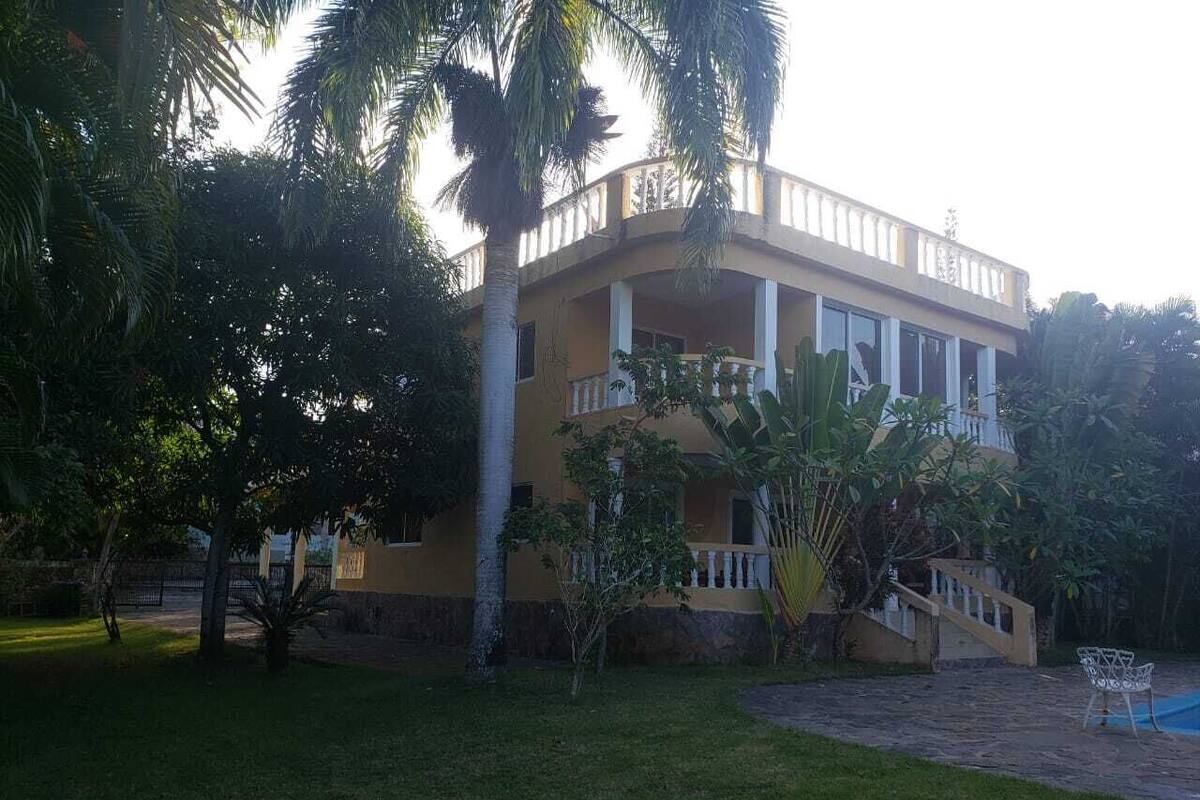 A two-story building with a balcony, surrounded by palm trees and a well-maintained lawn.